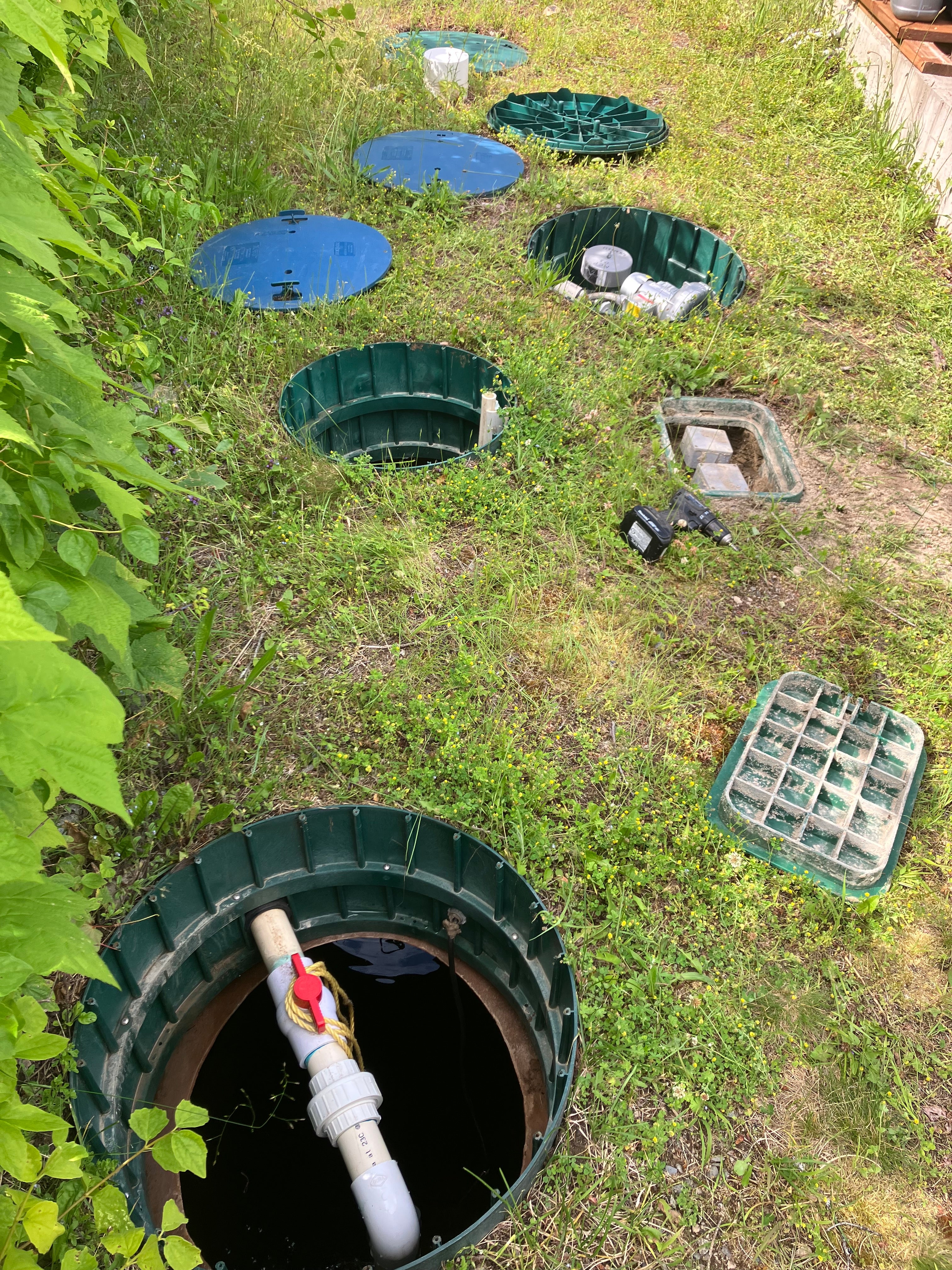 Top-down view of a septic tank inspection with tools and equipment on grass.